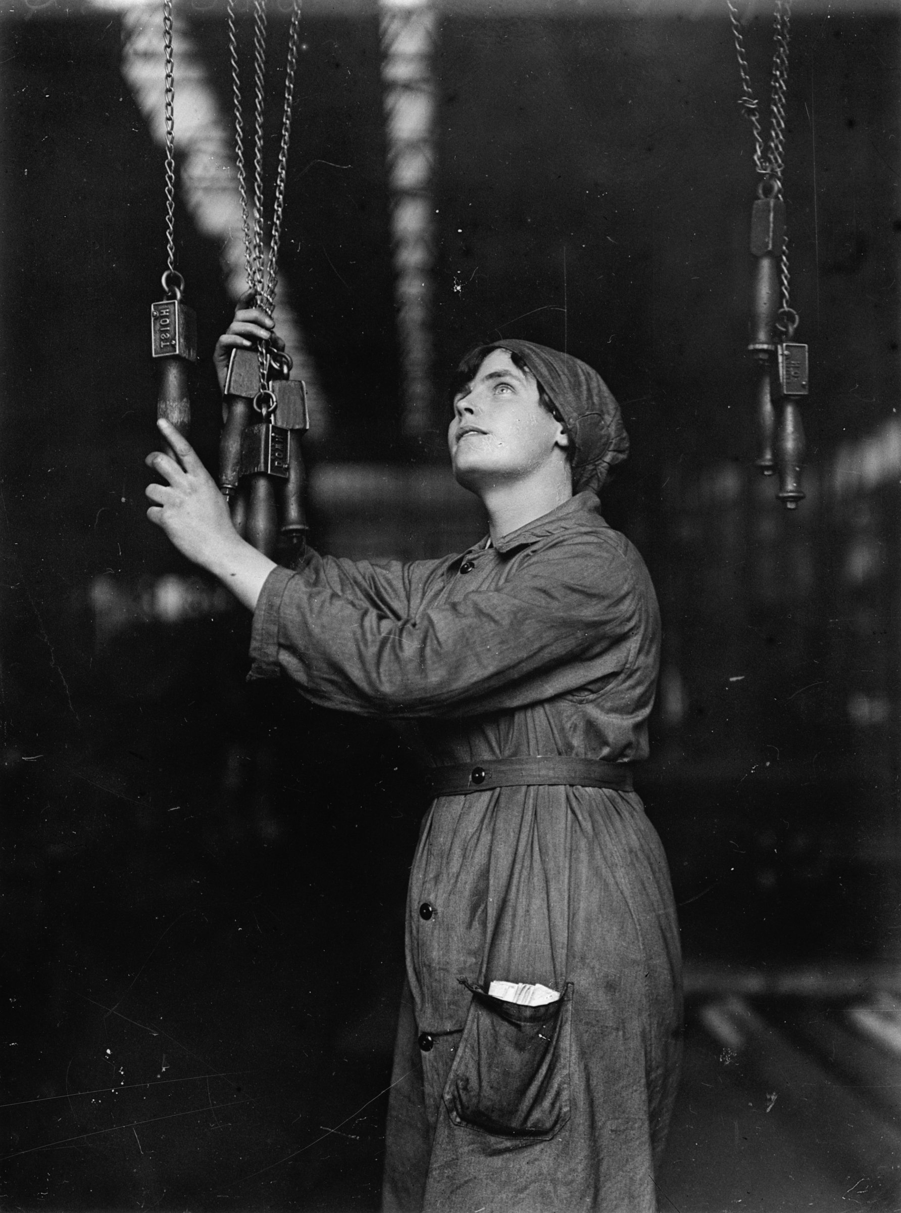 A female worker operating overhead electric cranes with key chains from the ground level in a shipbuilding yard. ©Crown Copyright.